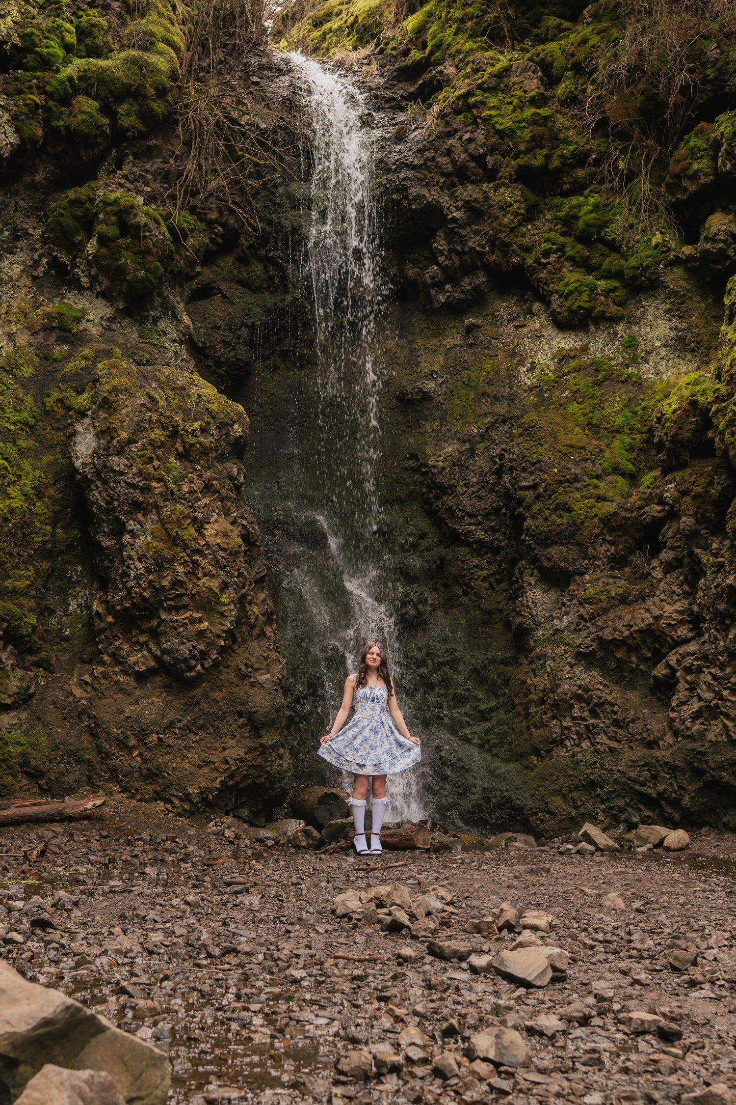 A waterfall cascades down moss-covered rocks in a scenic forest setting.