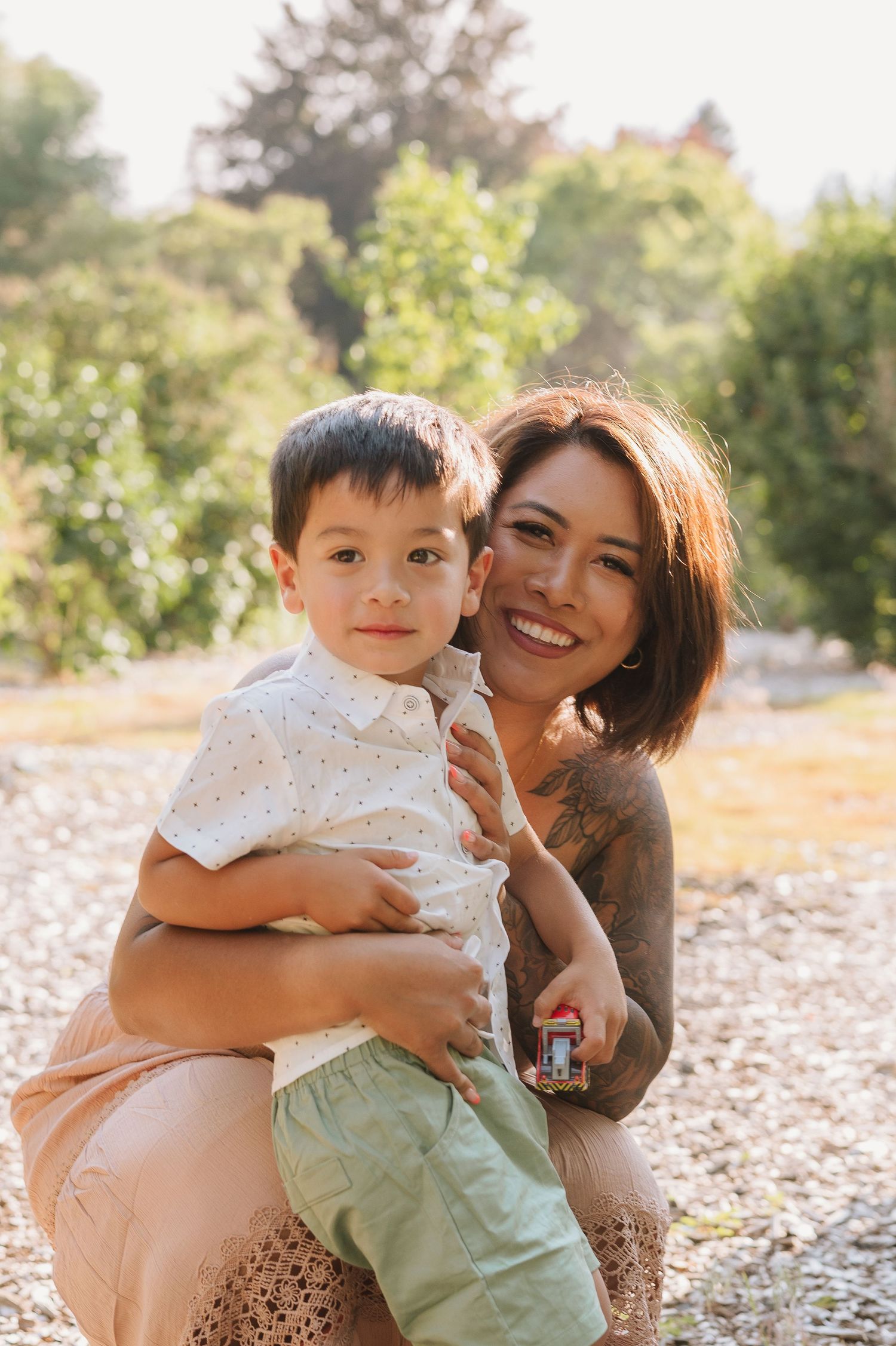 A tender outdoor portrait of a parent and child sharing a joyful moment together in a sunny natural setting.