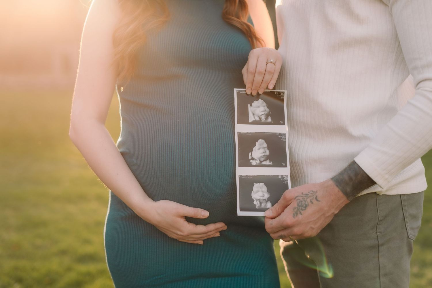 A couple holds an ultrasound photo during a sunset maternity photoshoot in a golden field.