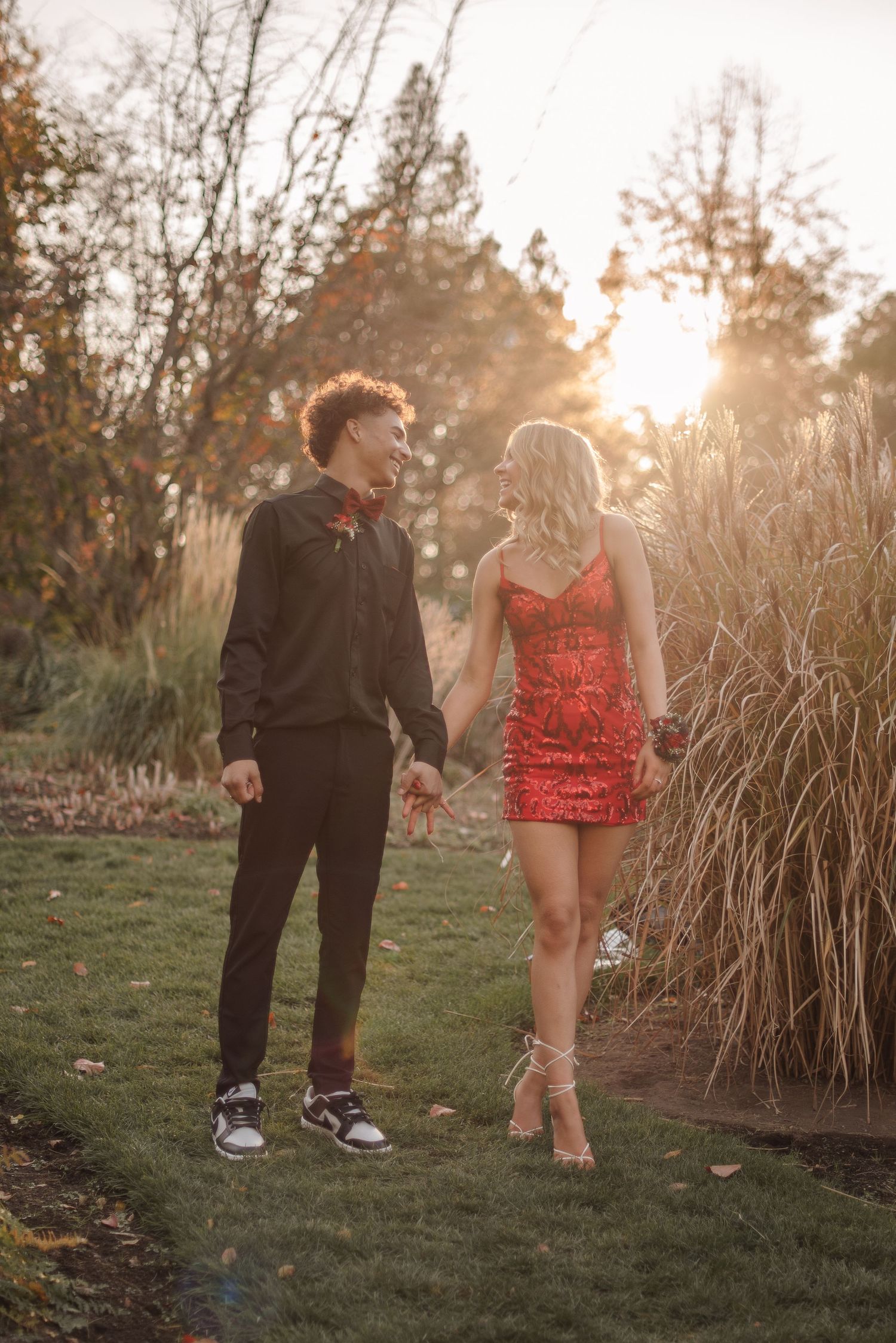 Two people in contrasting outfits walk together through tall grass at sunset creating a romantic silhouette.