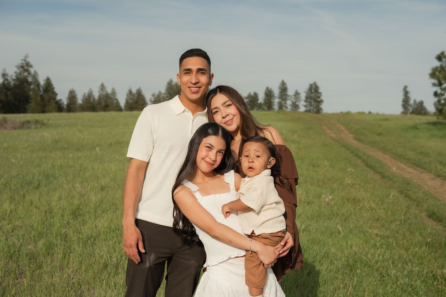 Happy family of four posing in a green meadow, parents smiling with two young children on a sunny day.