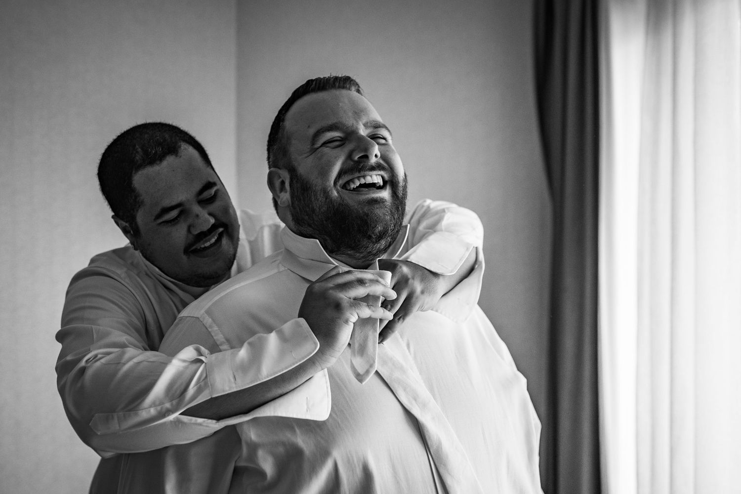twee bruidegommen die elkaar aankleden en lachen