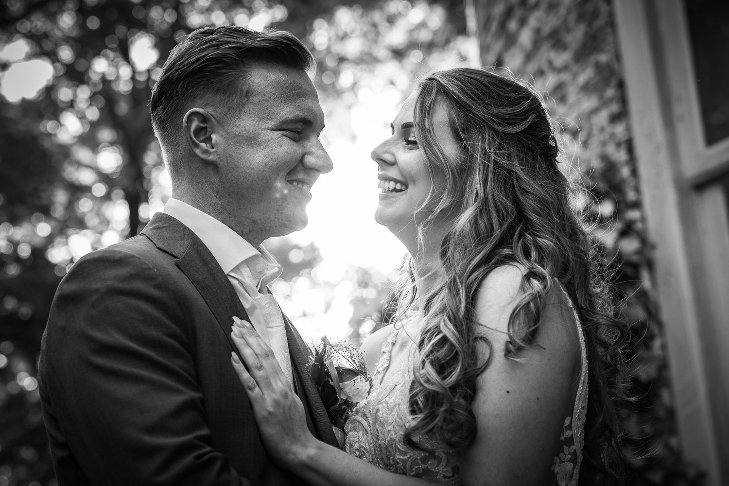 zwart wit foto van een blij bruidspaar die elkaar aankijken en lachen