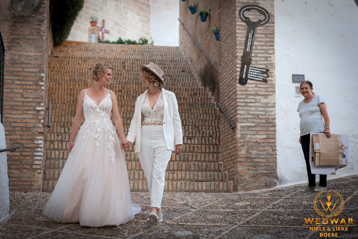 twee bruiden in spanje die weglopen met een vrouw die ze lachend na kijkt
