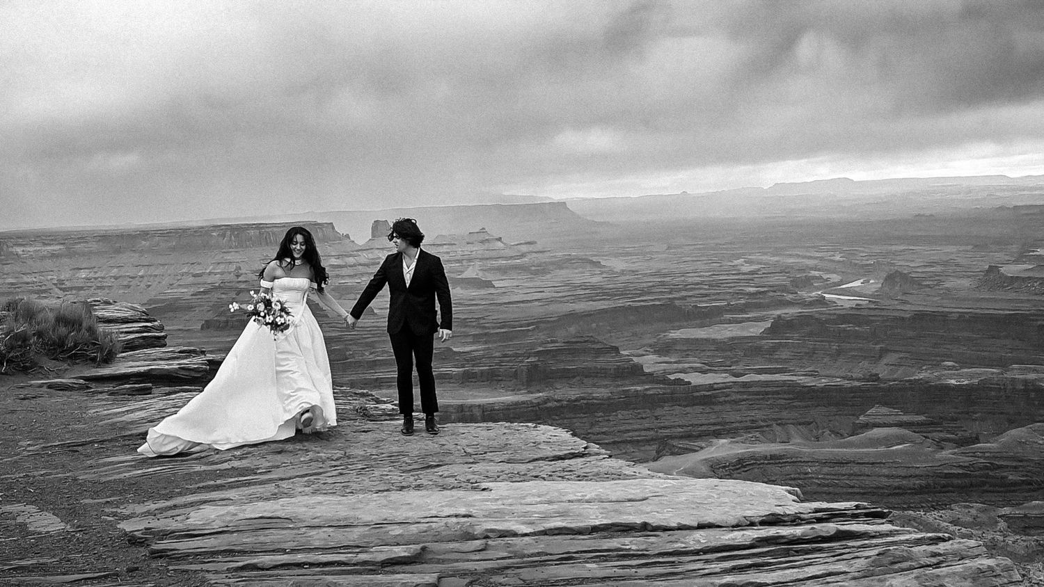 bride and groom holding hands walking on mesa at dead horse point in Moab Utah, cliffside elopement