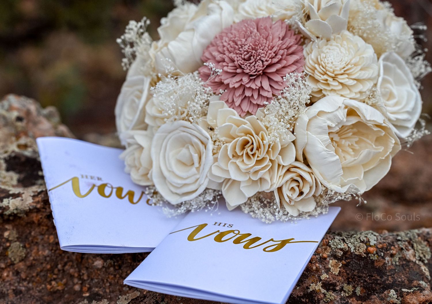 Wedding bouquet with white and blush pink roses alongside two 'vows' cards with gold lettering on white paper.