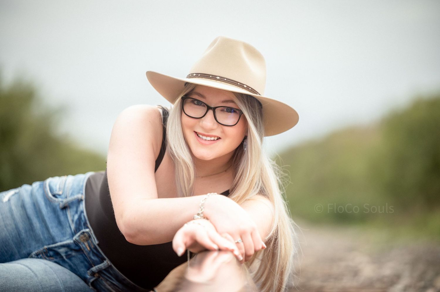 blonde cowgirl with blue eyes in stetson hat and jeans under moody skies