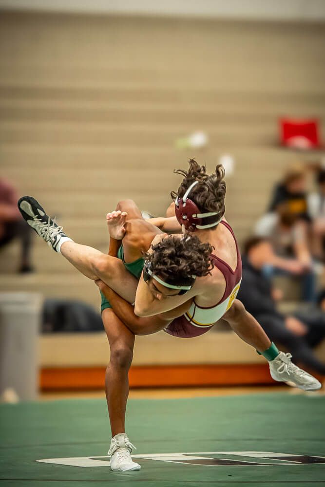Cheerleader performs high leg kick sequence in green uniform during indoor competition routine.