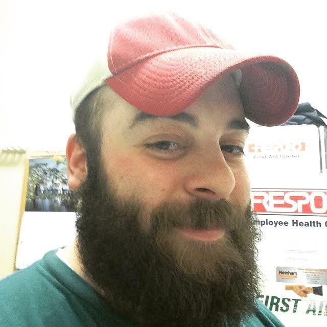 A selfie of someone wearing a pink baseball cap and green shirt with a full dark beard.