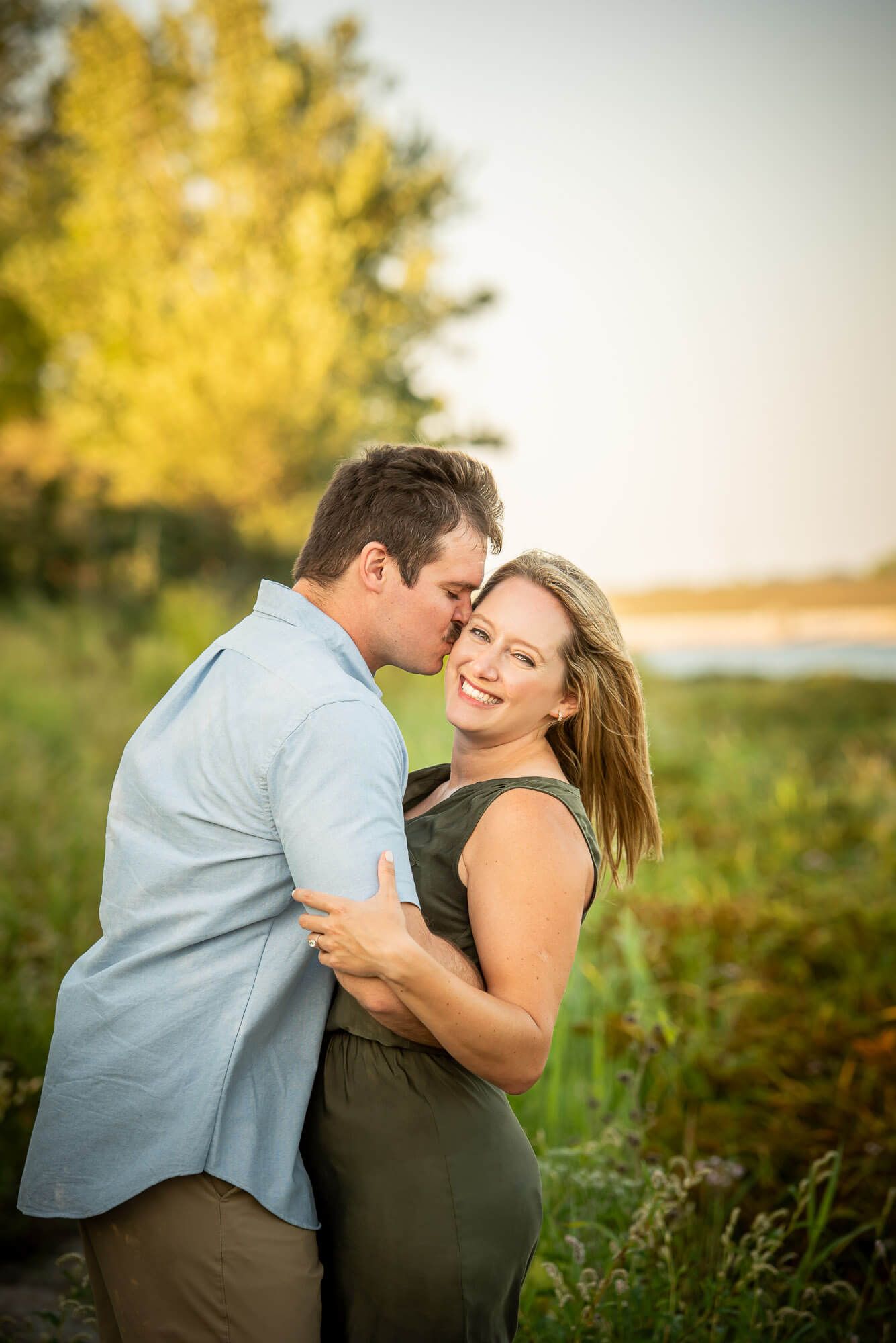A couple shares a romantic moment together in a field at sunset with golden light during couple's photography in Omaha at Lake Chalco.