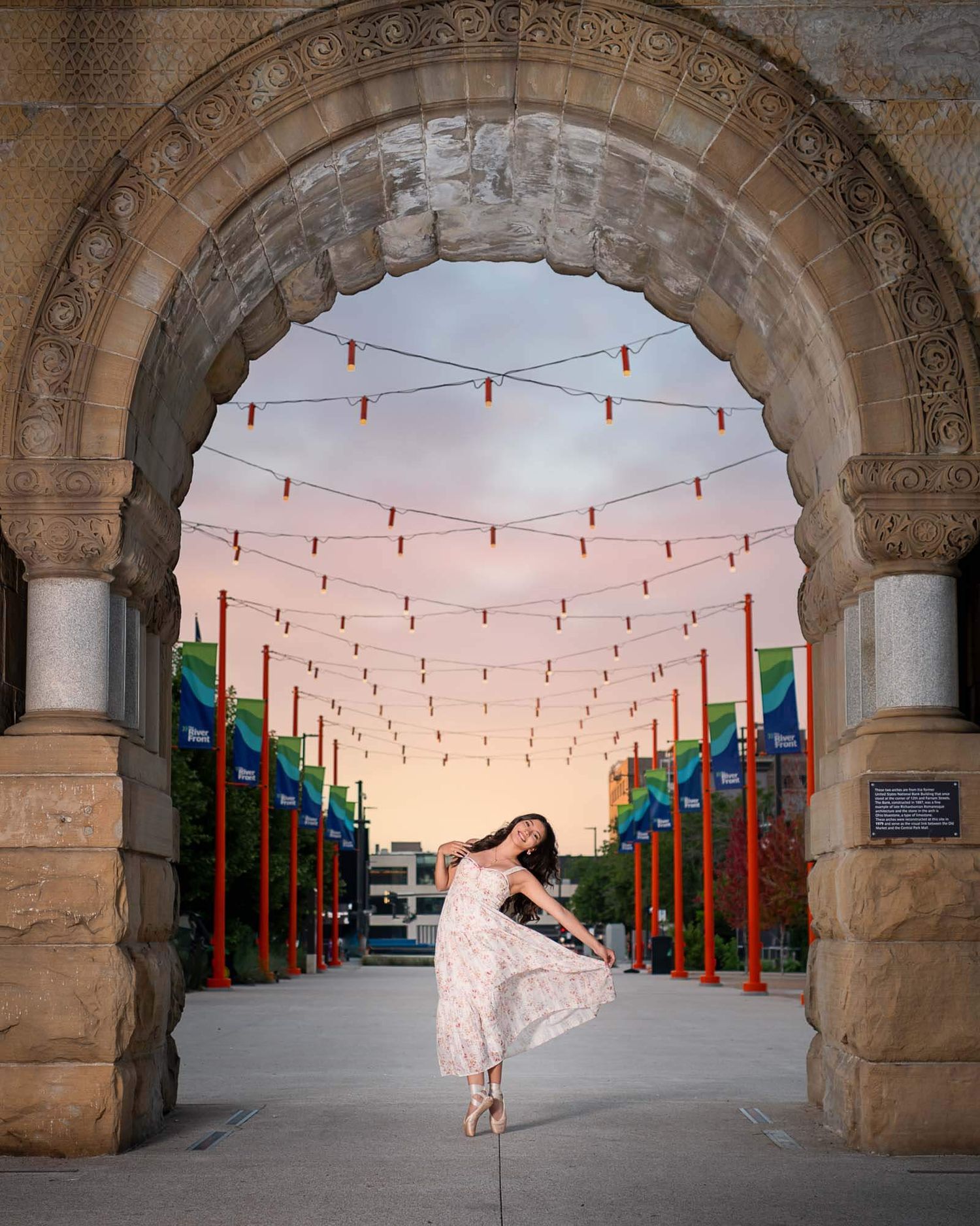Omaha senior photography of a female in a flowy floral dress in a dance move in Downtown Omaha at Gene Leahy Mall under the arch.