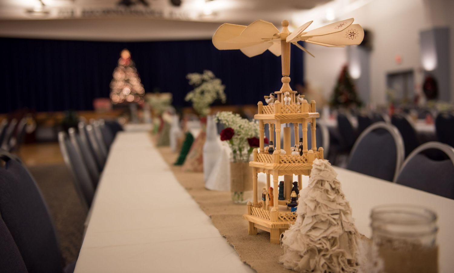Wooden pyramid centerpiece with burlap runner decorates a long banquet table at a holiday wedding reception.