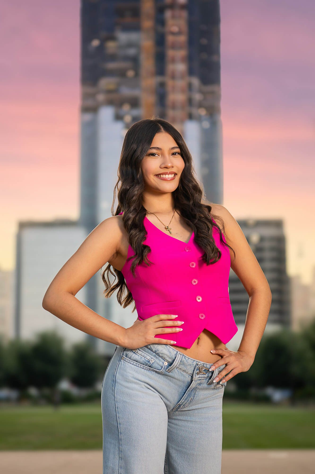 Fashion portraits at sunset featuring a hot pink top and light denim against an urban skyline backdrop.