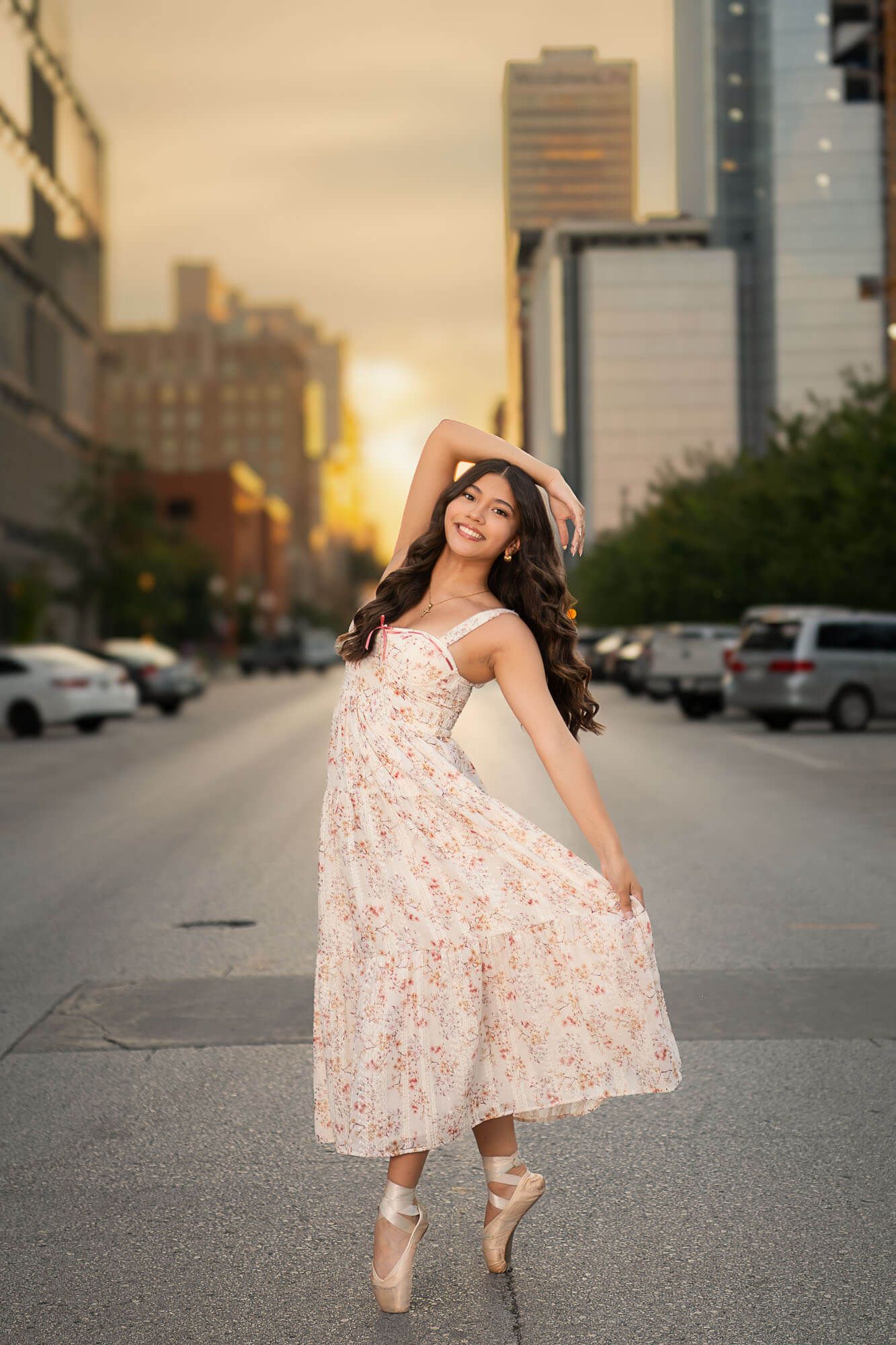 A ballet dancer performs an elegant pose on a city street at sunset wearing a romantic white dress.