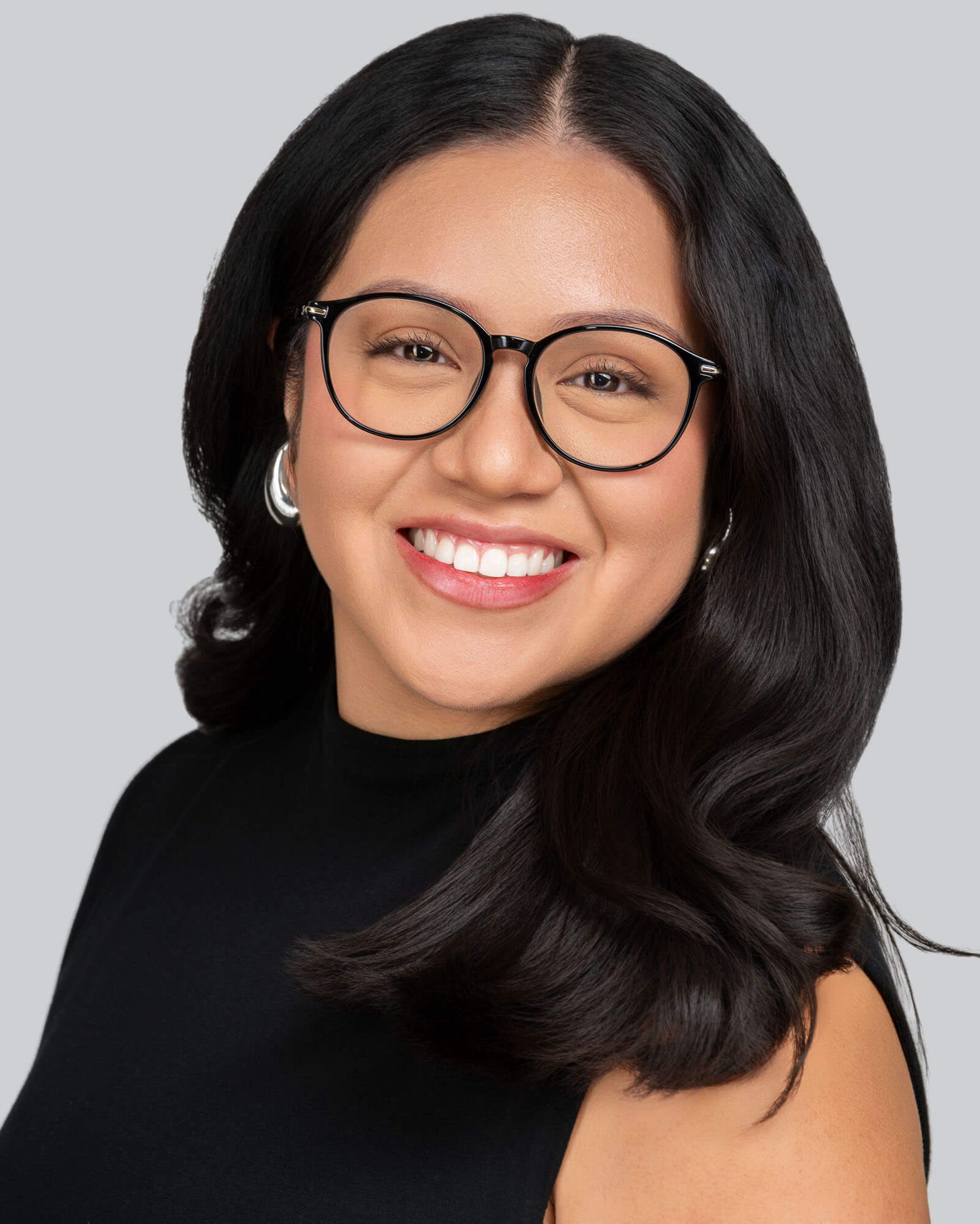 Professional headshot of a person in glasses and black top smiling against a gray background.