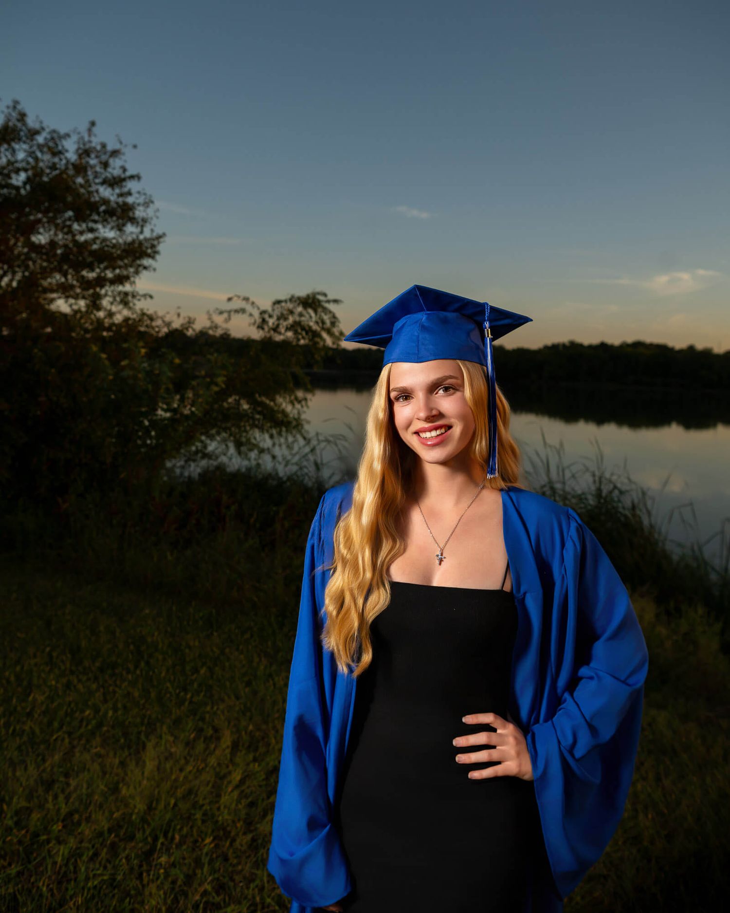 Sunset graduation photoshoot by a lake with blue academic regalia.