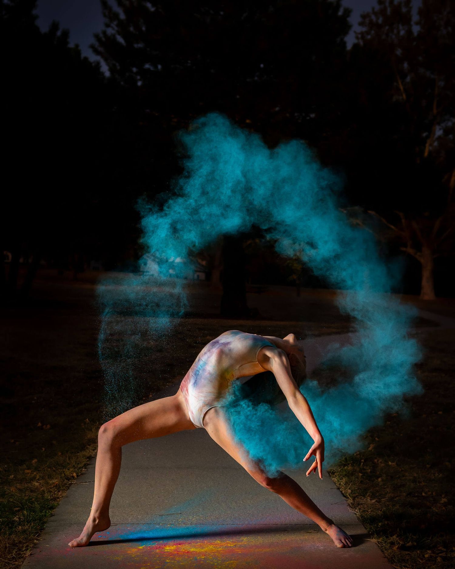 Artistic dance performance with blue powder effects creating ethereal motion trails in low light conditions.