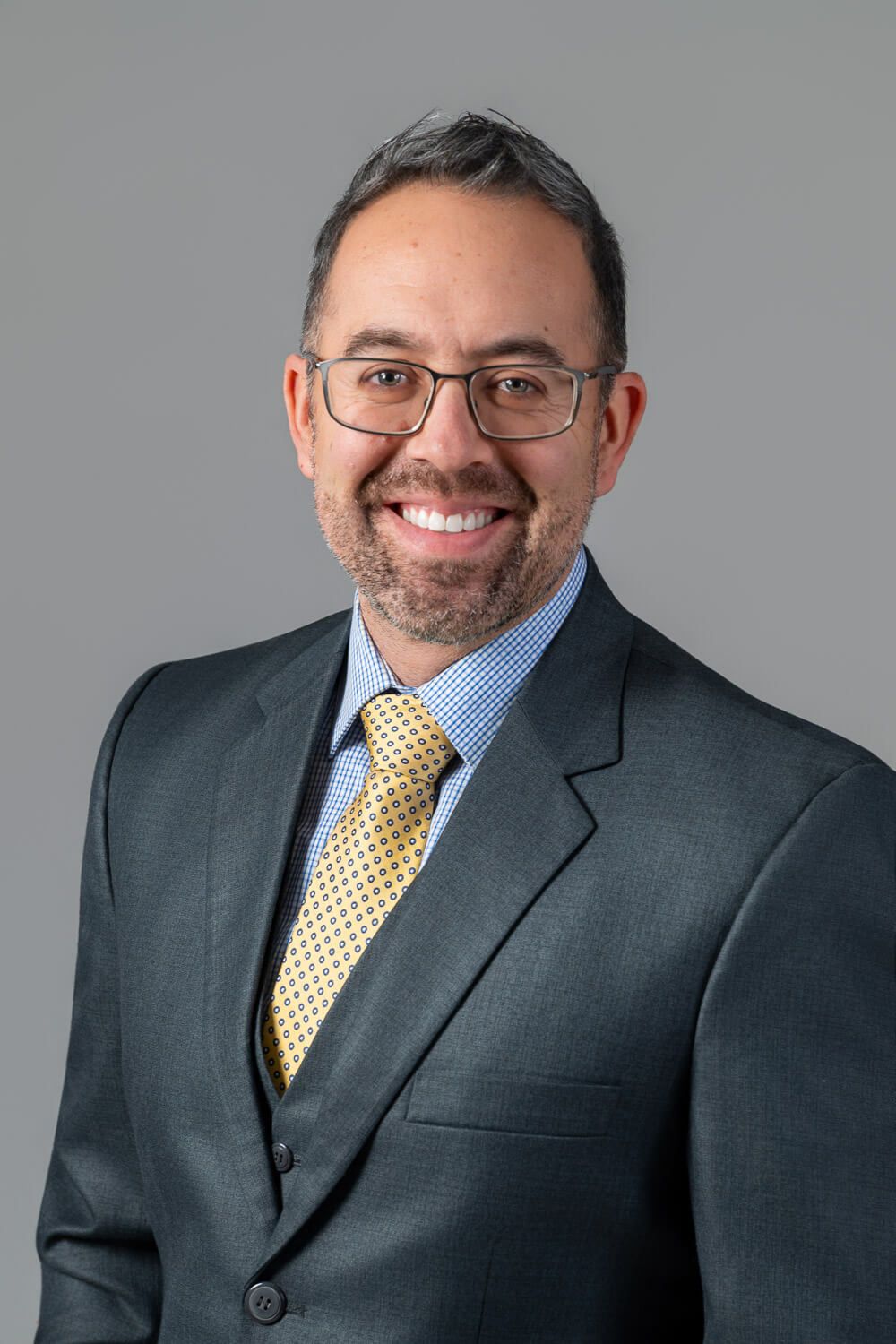 Professional headshot series of a person in business attire with glasses and yellow tie against a gray background.