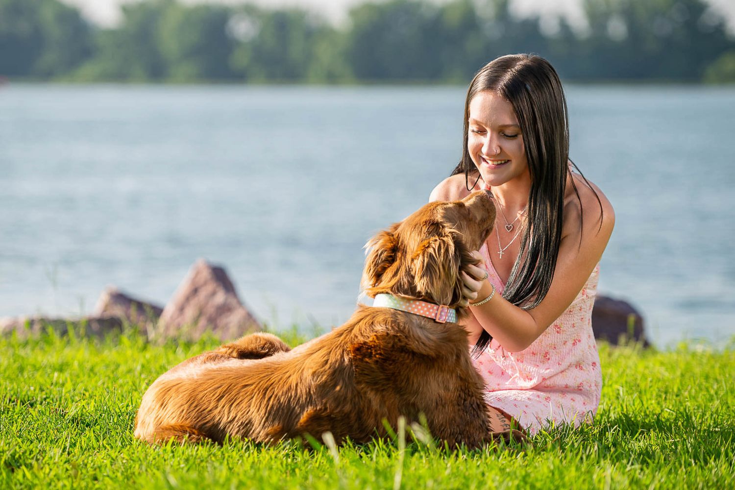 Norfolk High School senior and her dog sitting in the grass in front of a lake in Norfolk, NE.
