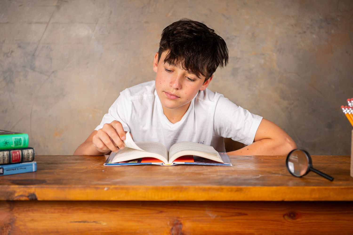 Student in white shirt concentrates while writing at wooden desk during class time.