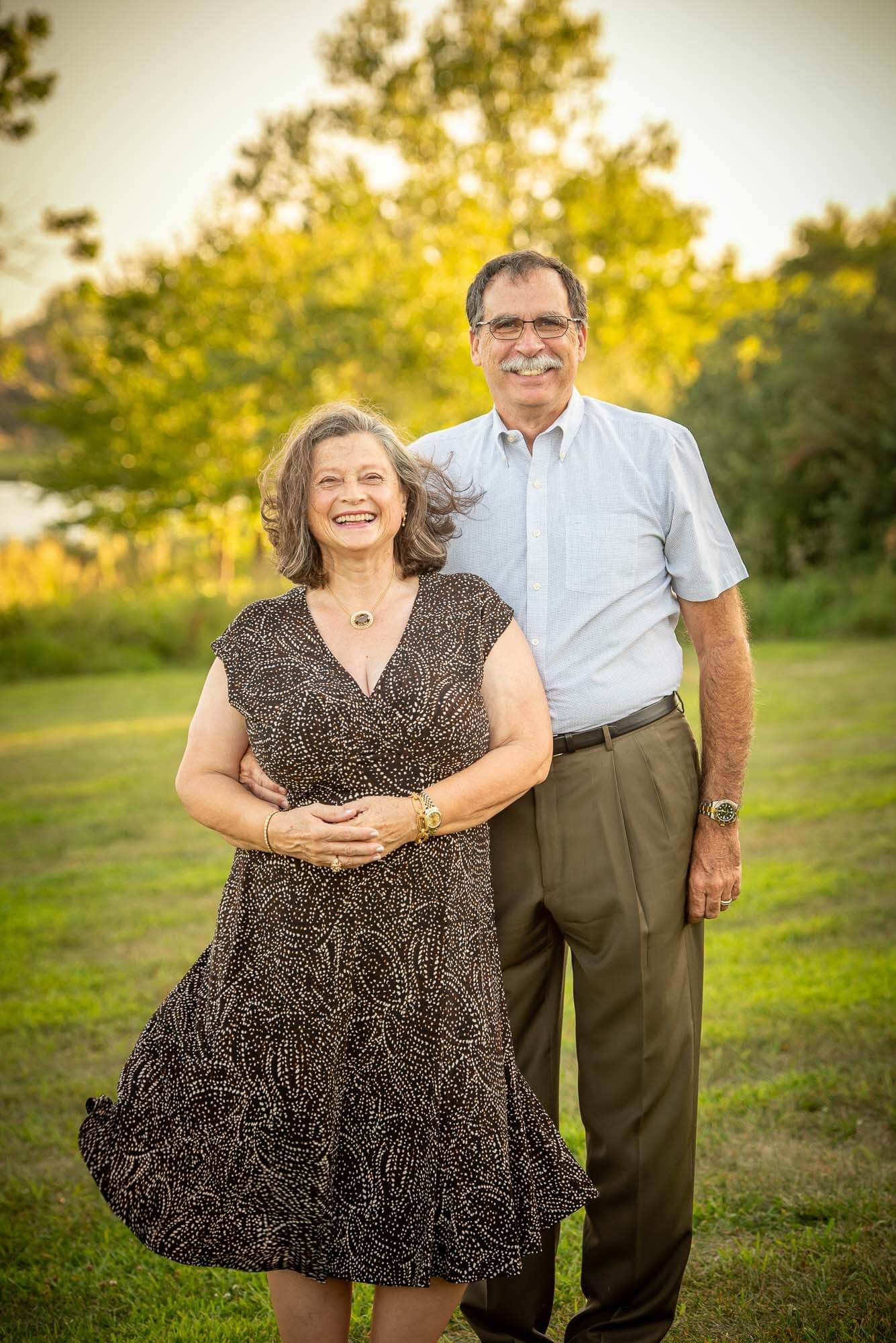 Couple posing playfully in a grassy field at sunset, showing joyful expressions.