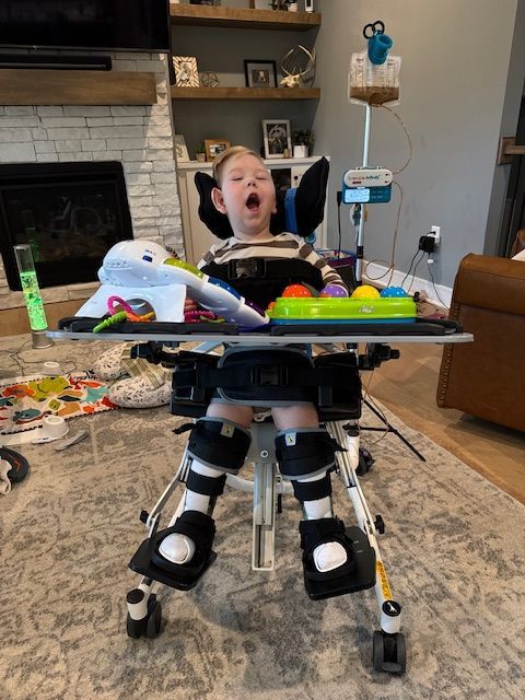 A medical chair with supplies and feeding equipment set up in a cozy living room with a stone fireplace and wooden shelves.
