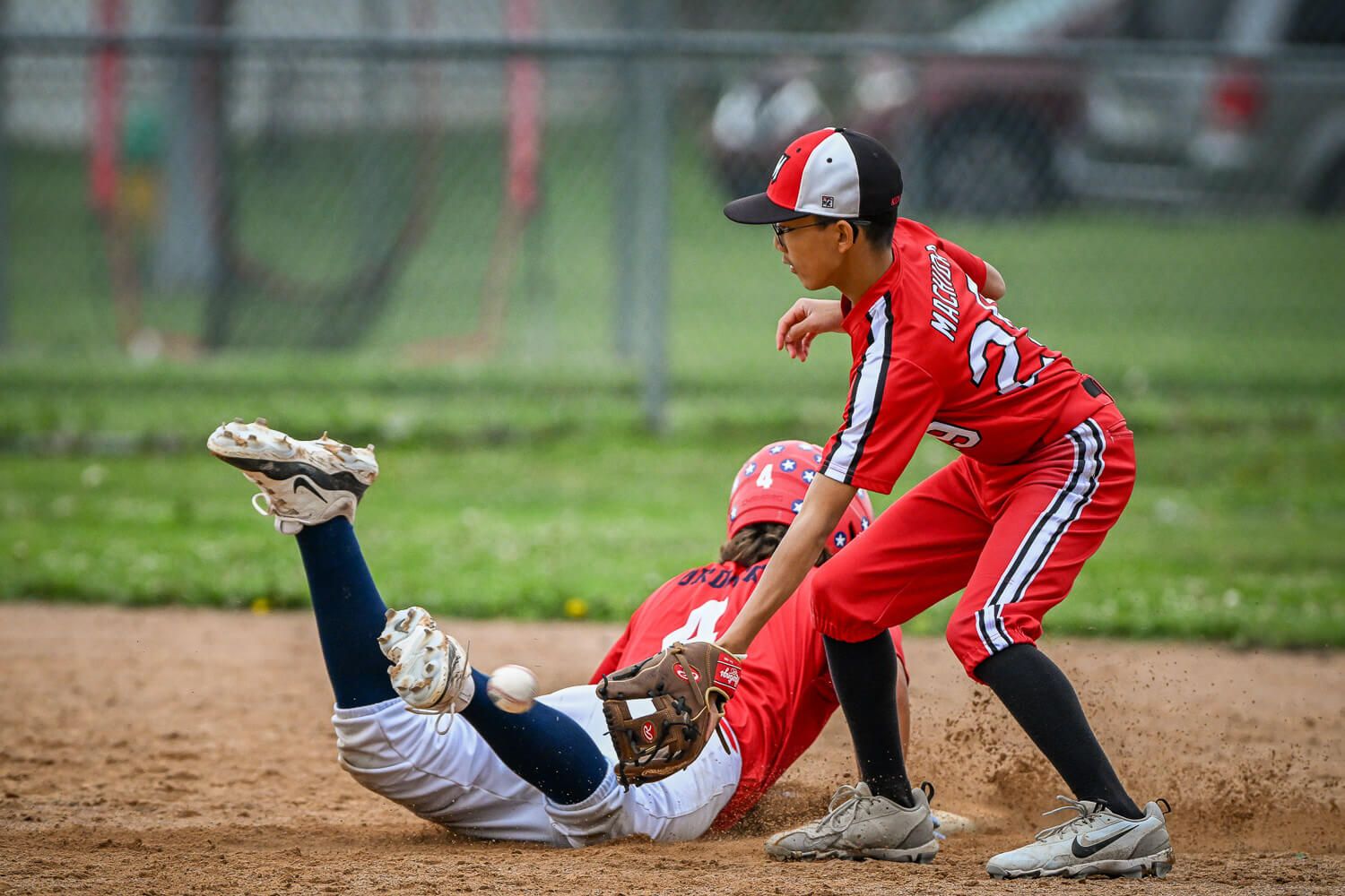 Baseball player in red uniform slides into base during competitive game while opponent attempts to make the tag.