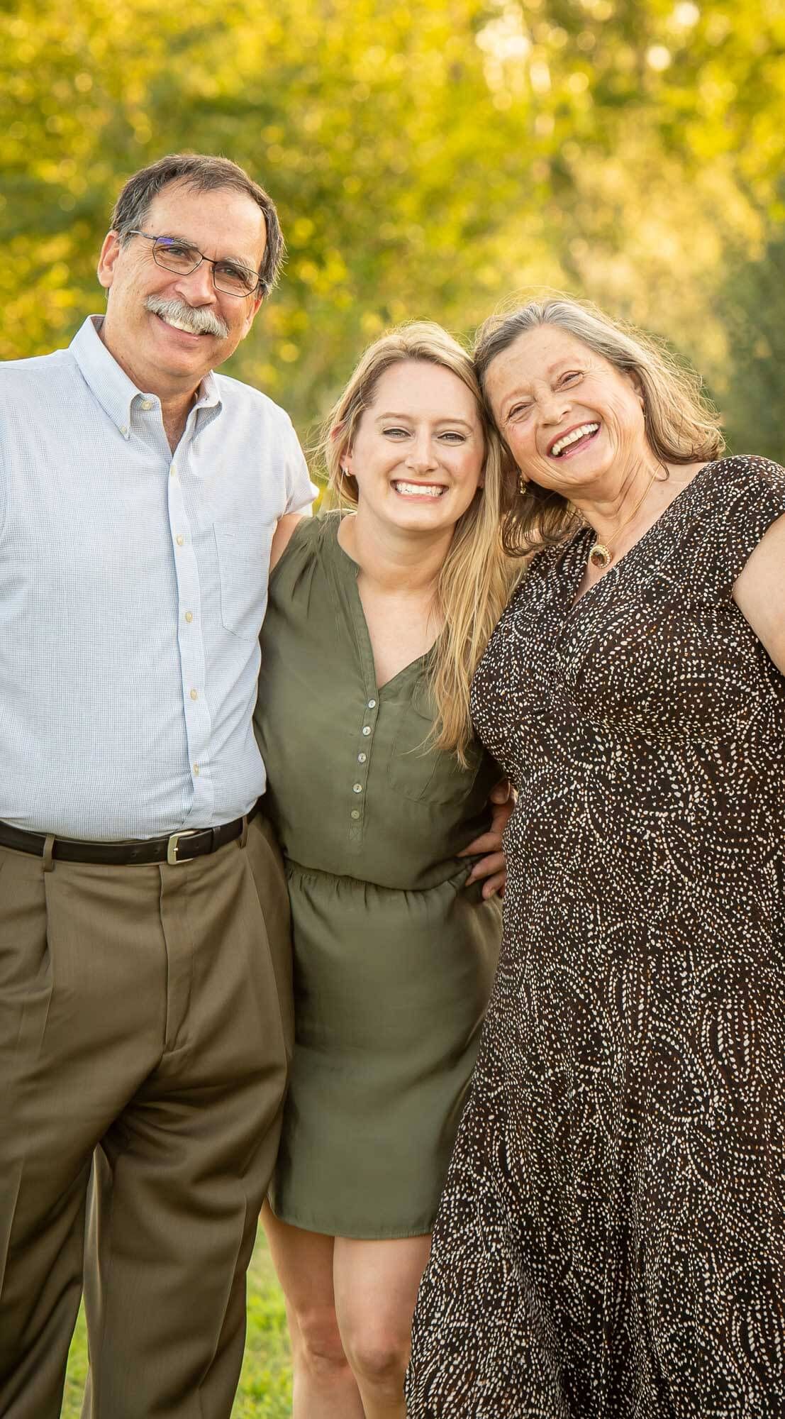 Three people share joyful laughter together outdoors with golden sunlit trees in the background.