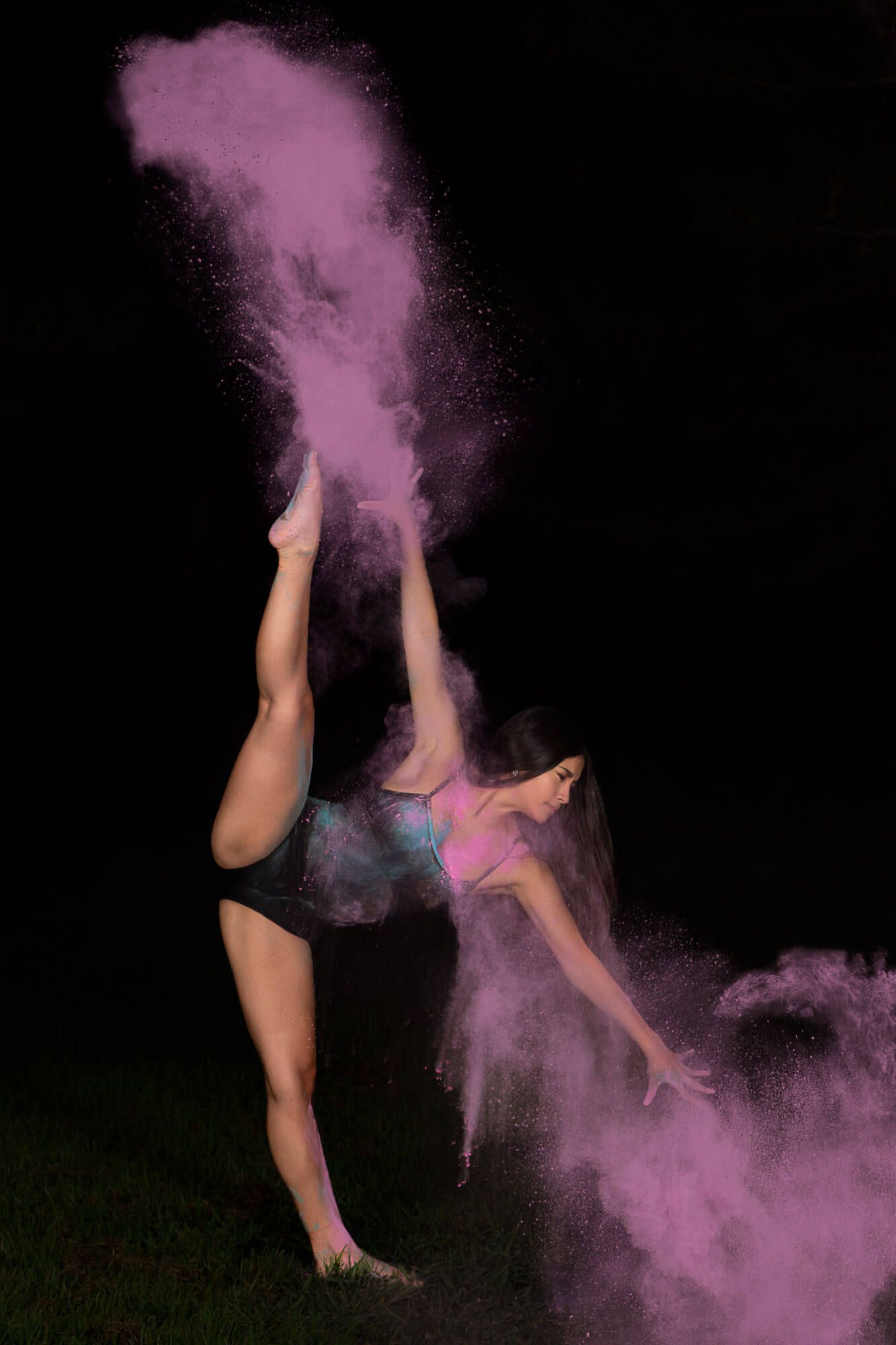 Dancer performs a high kick with pink powder creating dramatic effect against dark background.