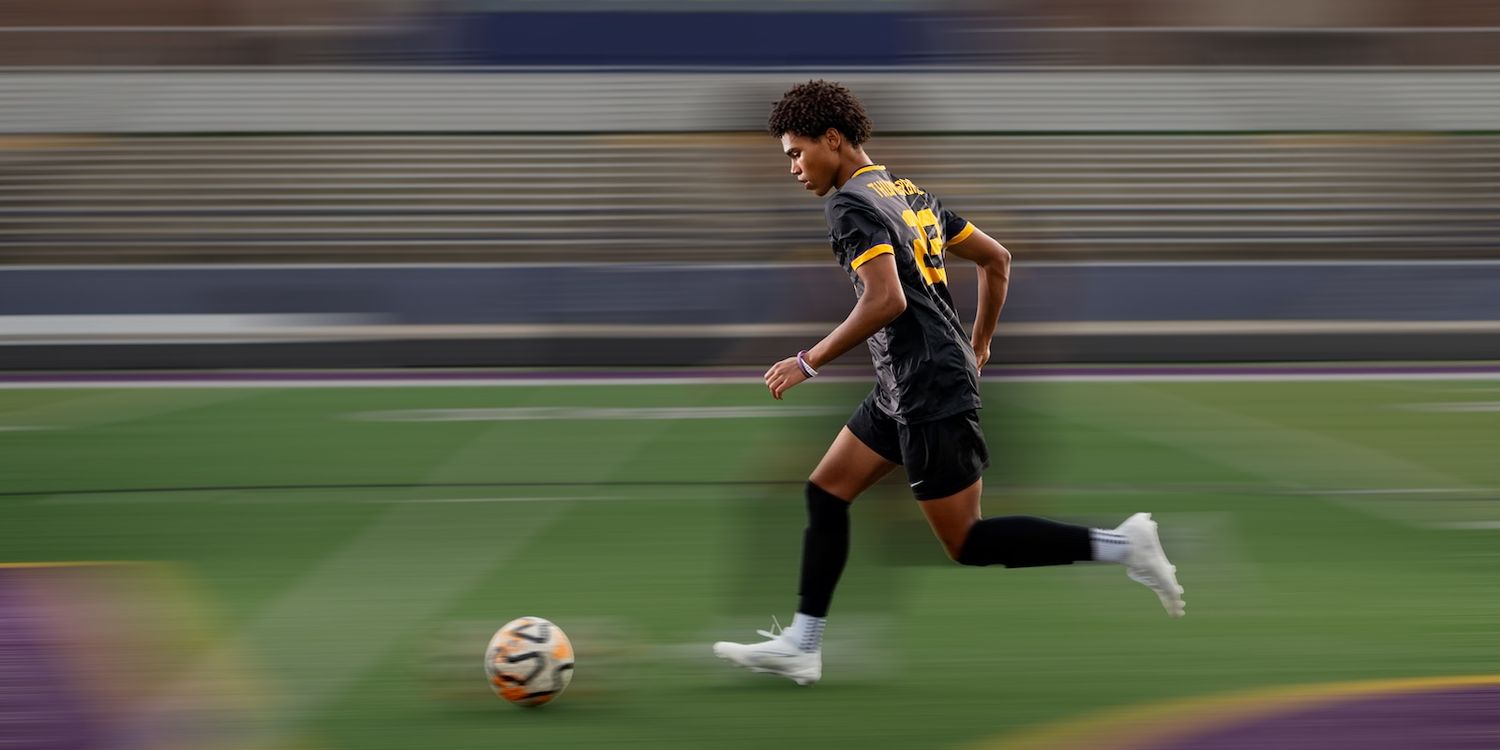 Omaha senior soccer player runs with the ball in a photographic composite on a professional field under stadium lights.