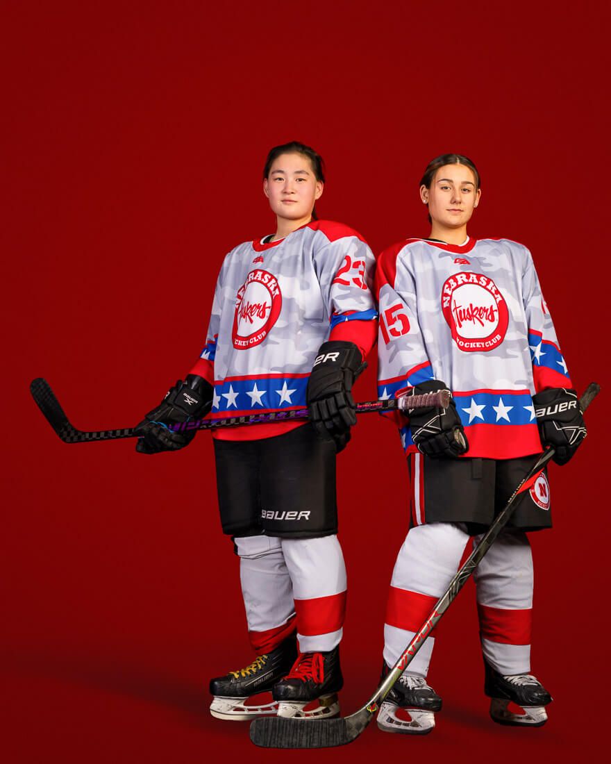 Youth hockey players in white and red jerseys with stars pose together against a red backdrop.
