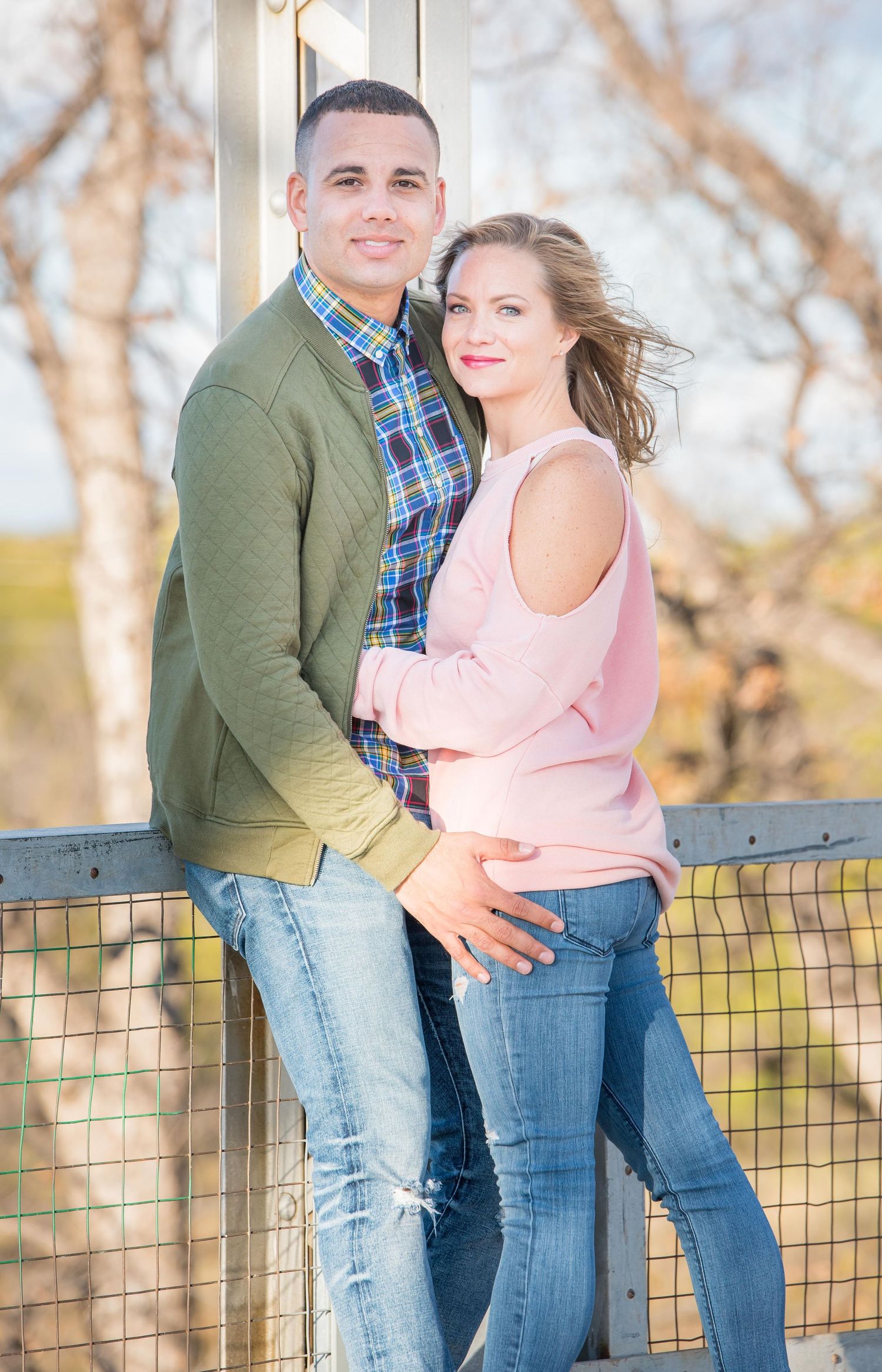 A romantic couple embraces on a wooden deck during an outdoor photoshoot at sunset.