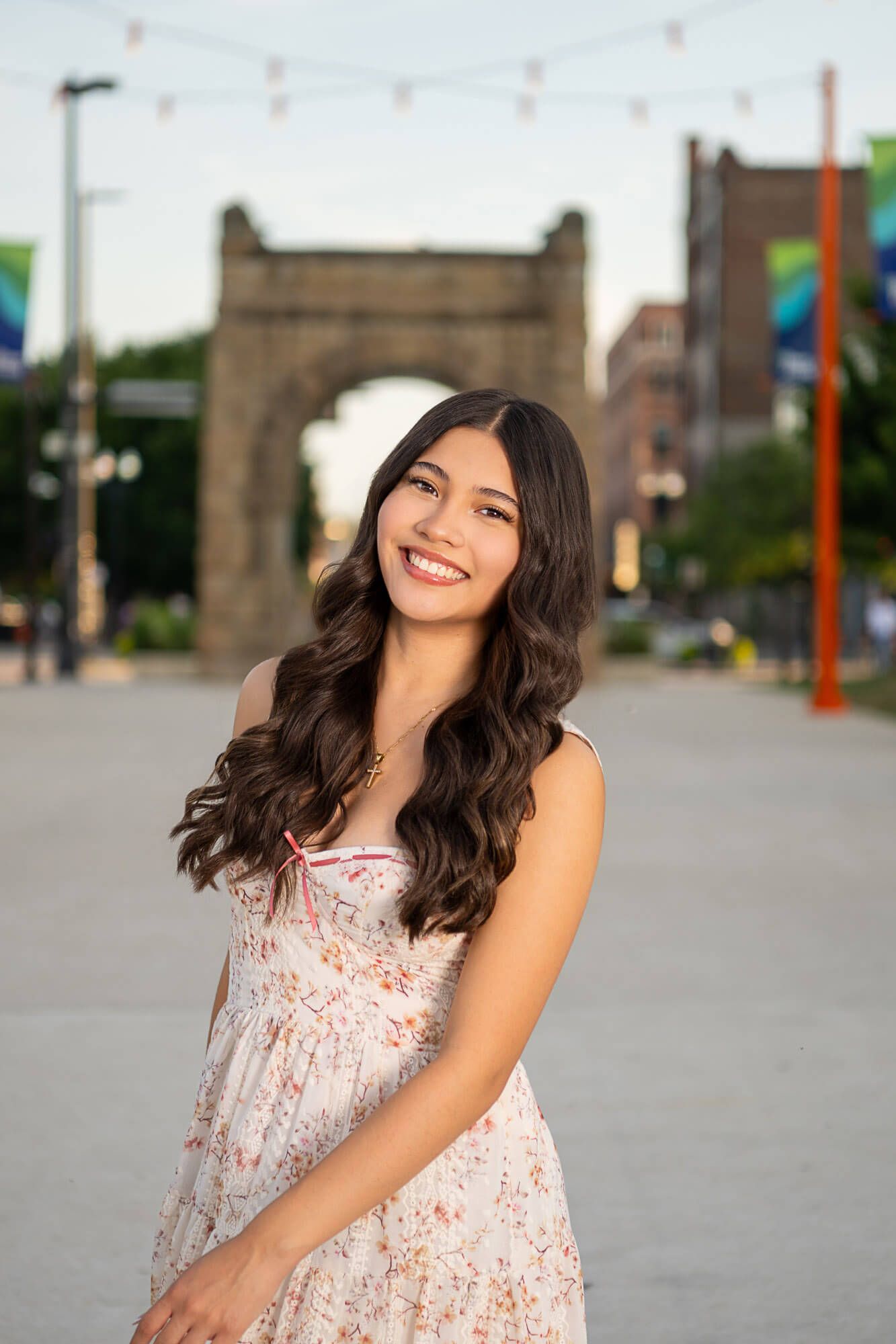 A summer portrait in a floral dress against an urban backdrop with a historic bridge in the background.