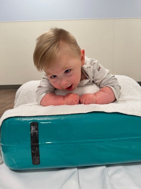 Small child lying on white towel looking down at turquoise vintage-style suitcase or luggage piece.