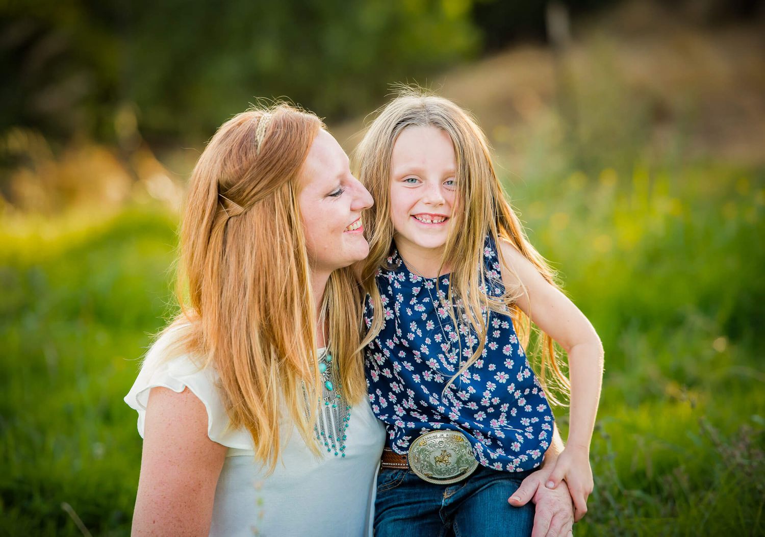Two people share joyful moments together in a sunlit outdoor setting with natural greenery in the background.