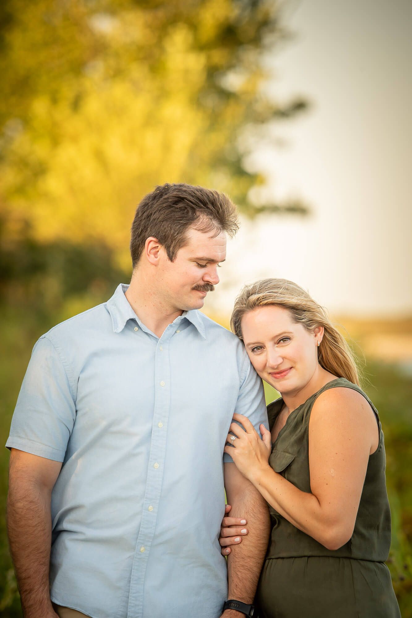 A couple shares tender moments outdoors during a golden hour photoshoot in a natural setting.