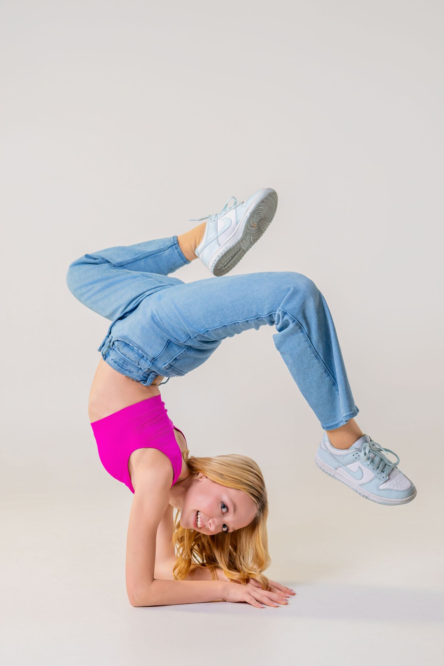 Omaha Senior Photography - Photographer in Omaha - Dancer performs acrobatic backbend in blue jeans and pink top against white background.