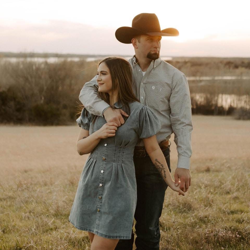 A couple embraces in a romantic sunset photoshoot on a rustic hillside wearing denim and cowboy style clothing.