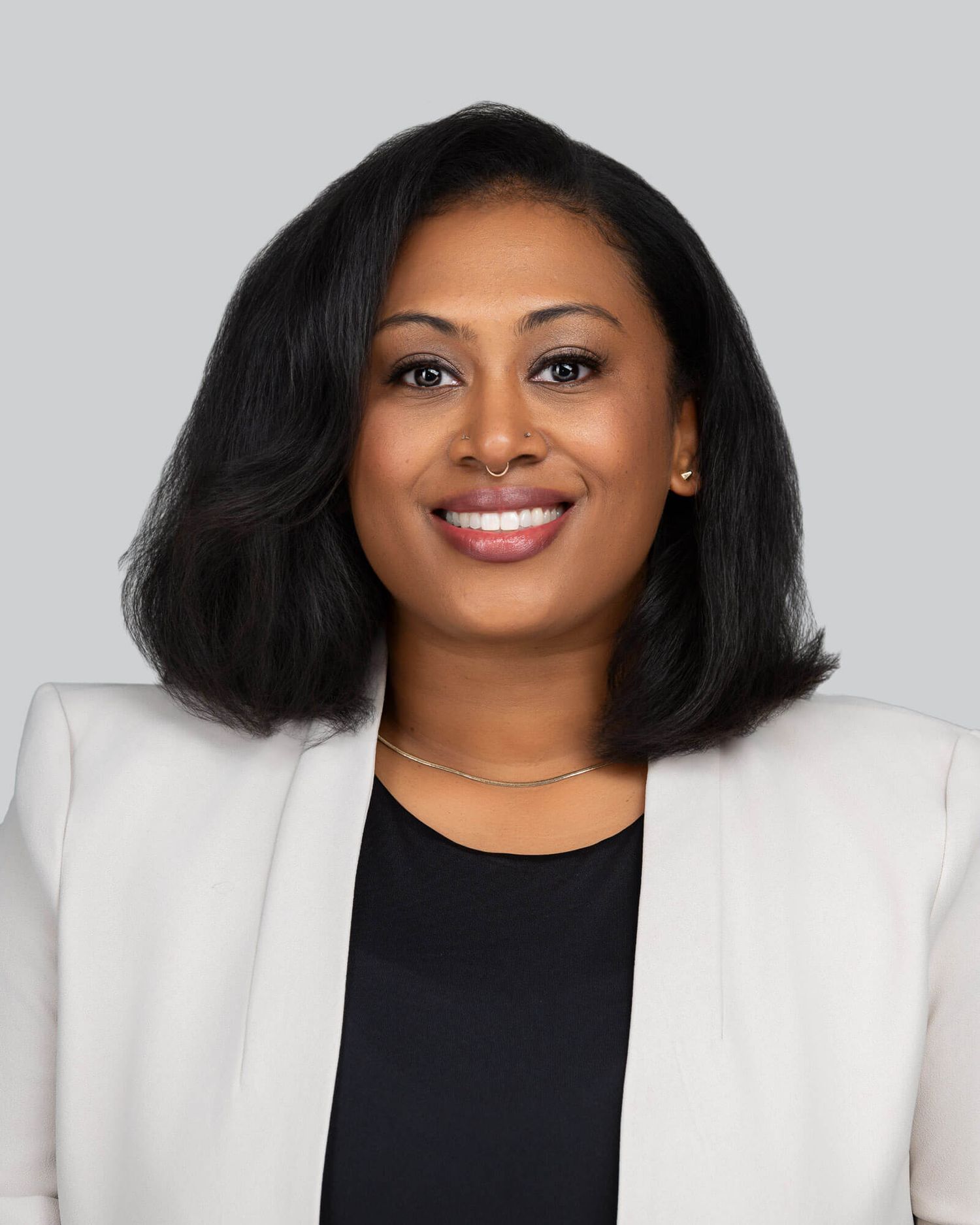 Professional business portrait of someone in a white blazer and black top against a light background.