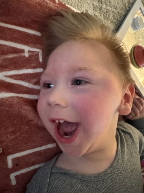 A child laying on a surface with an excited expression and wearing a gray shirt.