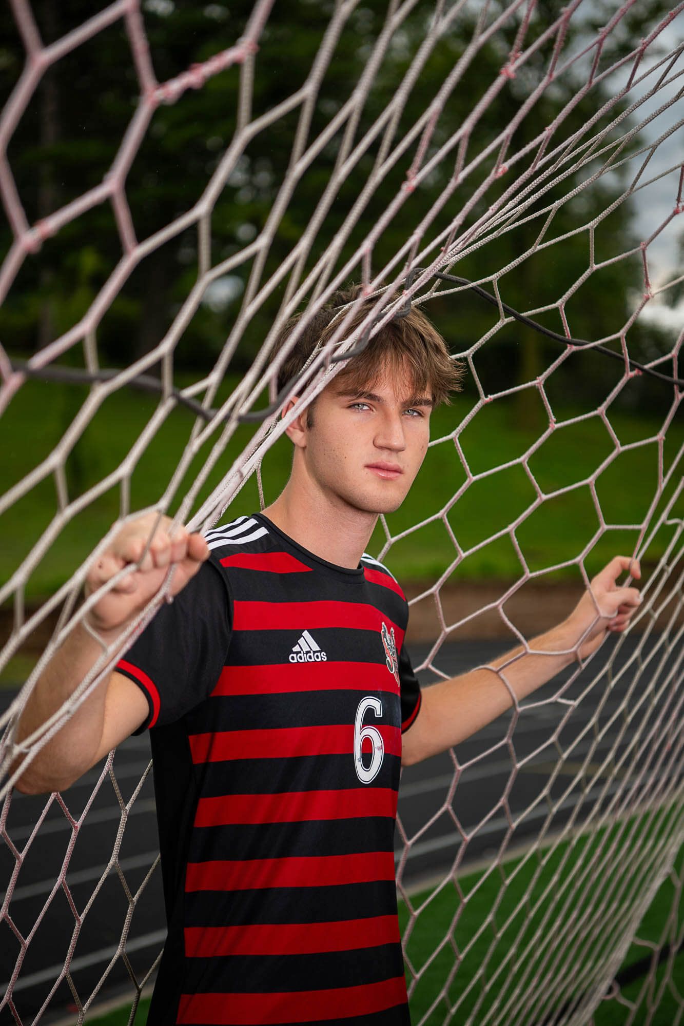 Soccer player in red and black striped jersey poses with goal net during outdoor photo session.