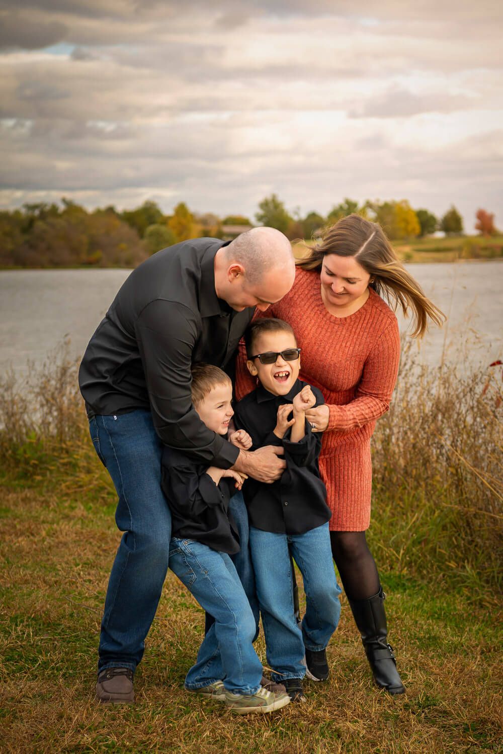 A family shares joyful moments together by a lake during an autumn outdoor photo session.
