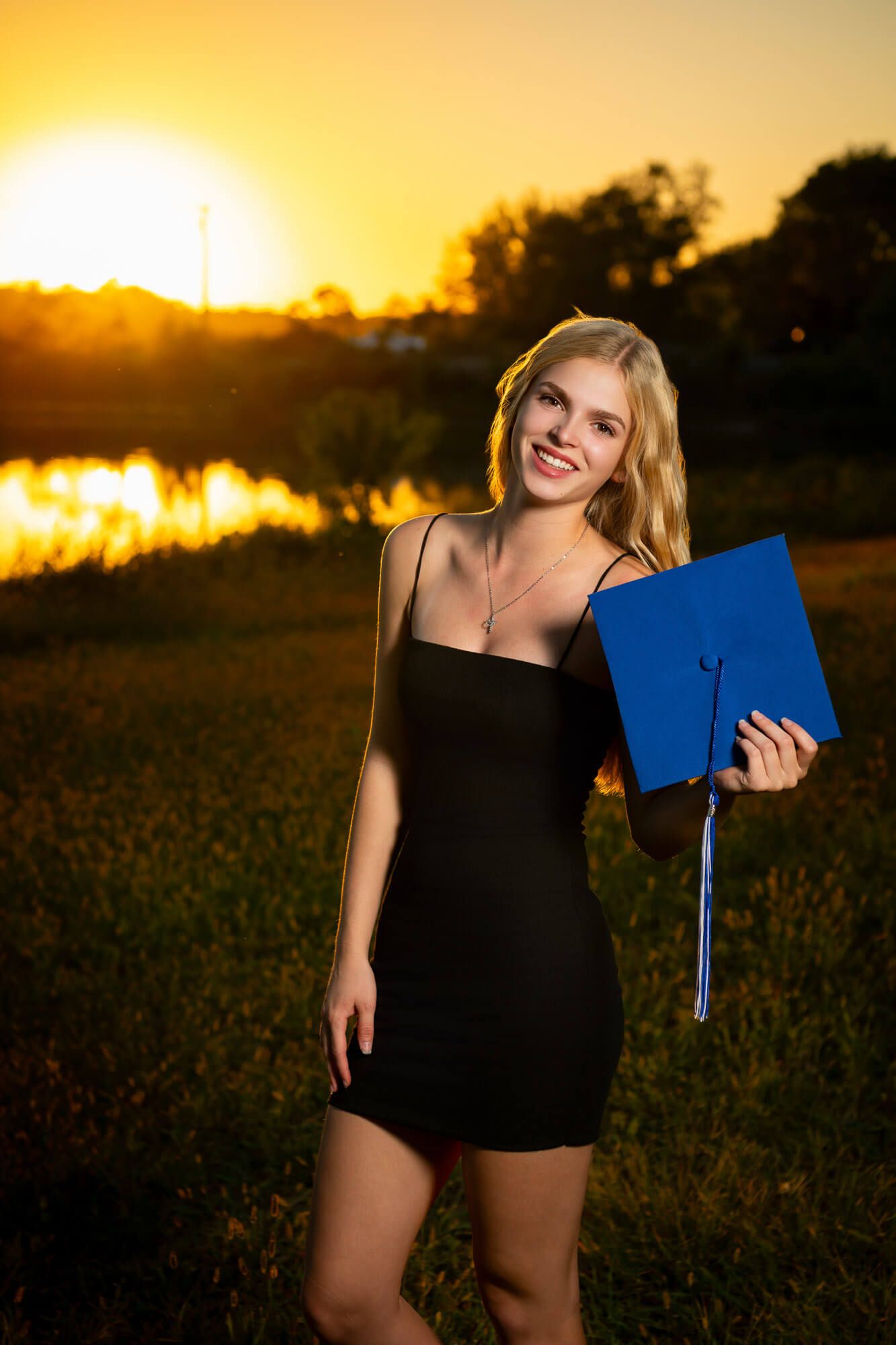 Golden hour graduation photos with blue diploma holder in a field setting.