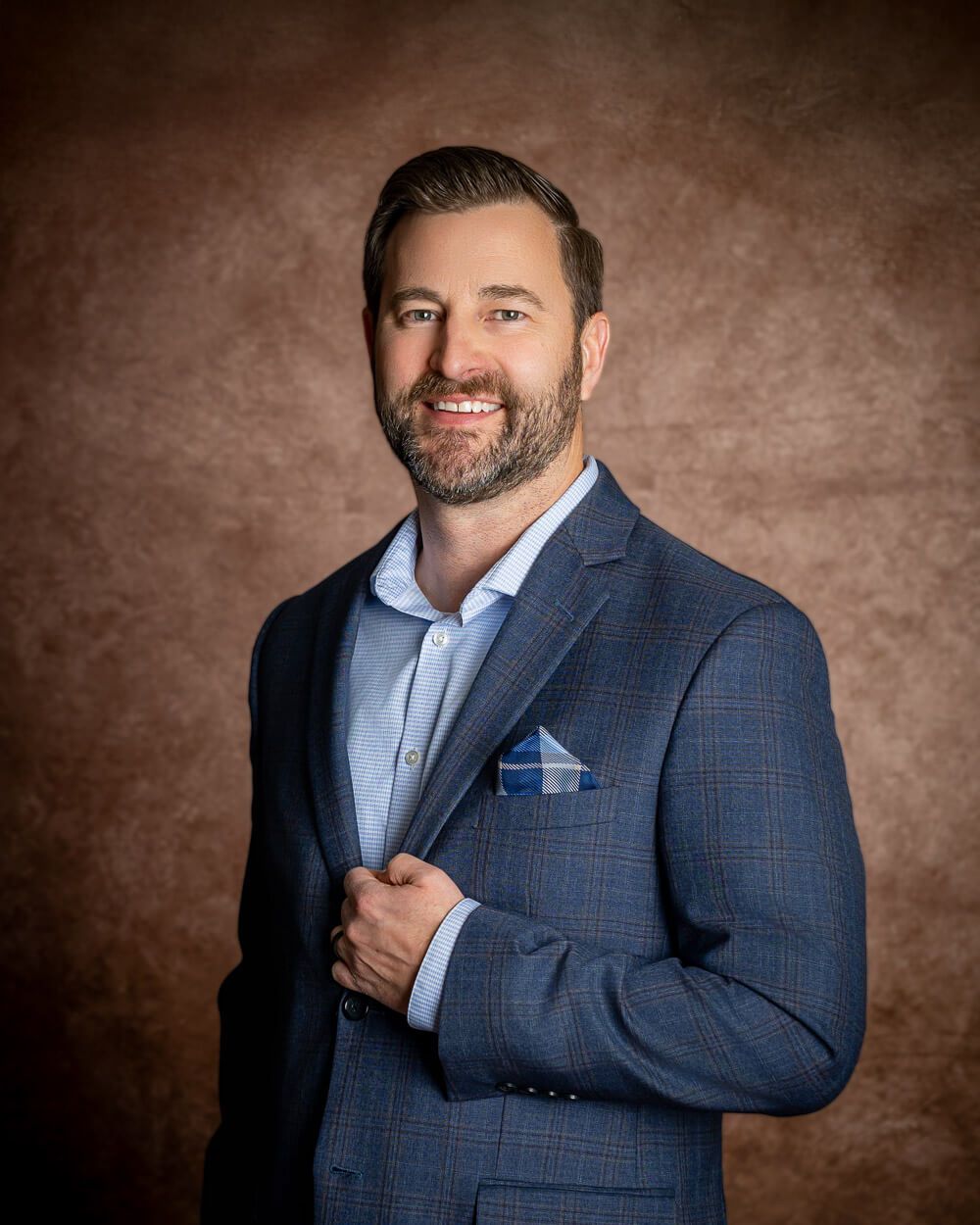 Professional headshot series showing a person in a navy checkered blazer with light blue pocket square against brown backdrop.
