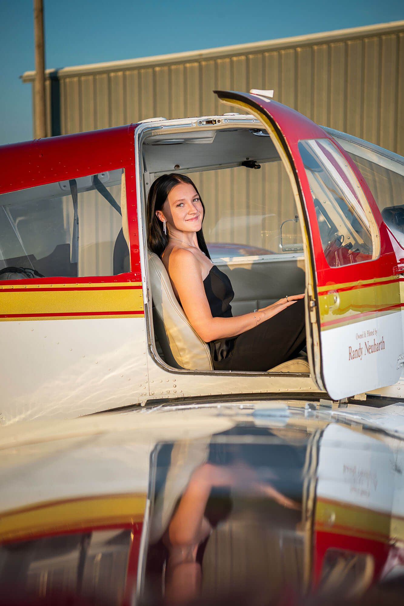 Small aircraft pilot sits in cockpit of red and white private plane during sunset.