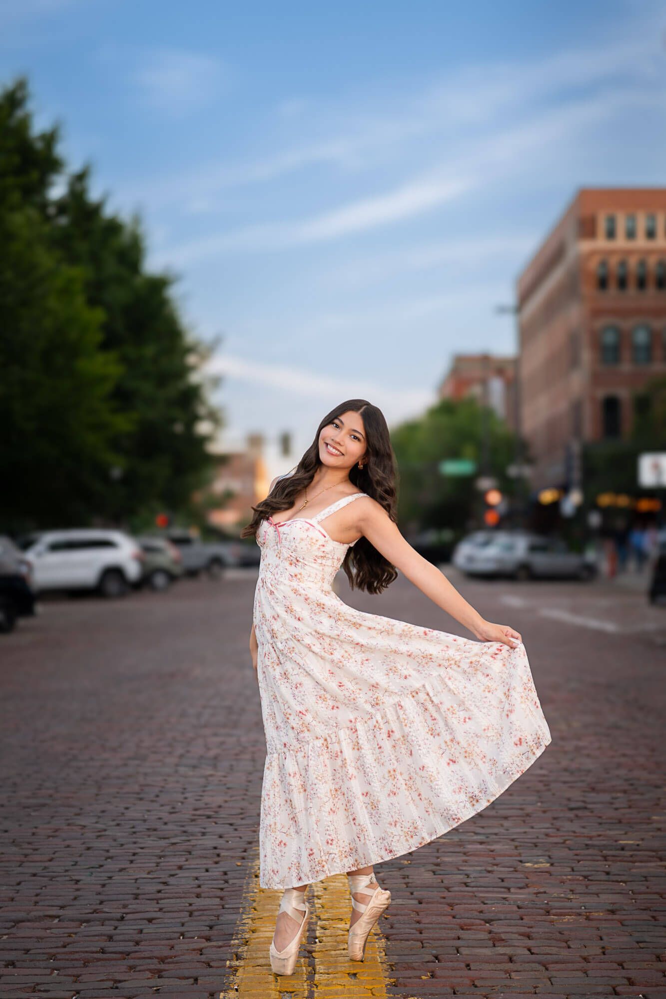 Dancing on cobblestone streets in a flowing white lace dress with brick buildings and blue sky in the background.