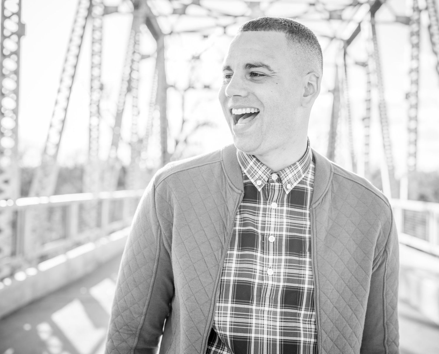 Black and white photo of someone wearing a plaid shirt and cardigan laughing joyfully while standing on a bridge Omaha family photographer.