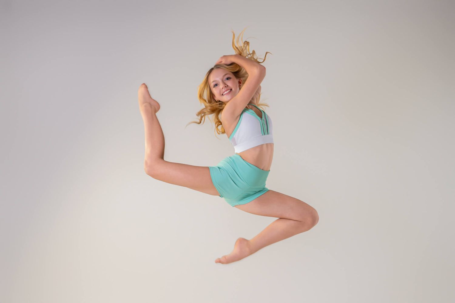 A graceful dancer performs a dynamic split leap sequence against a light gray studio backdrop.