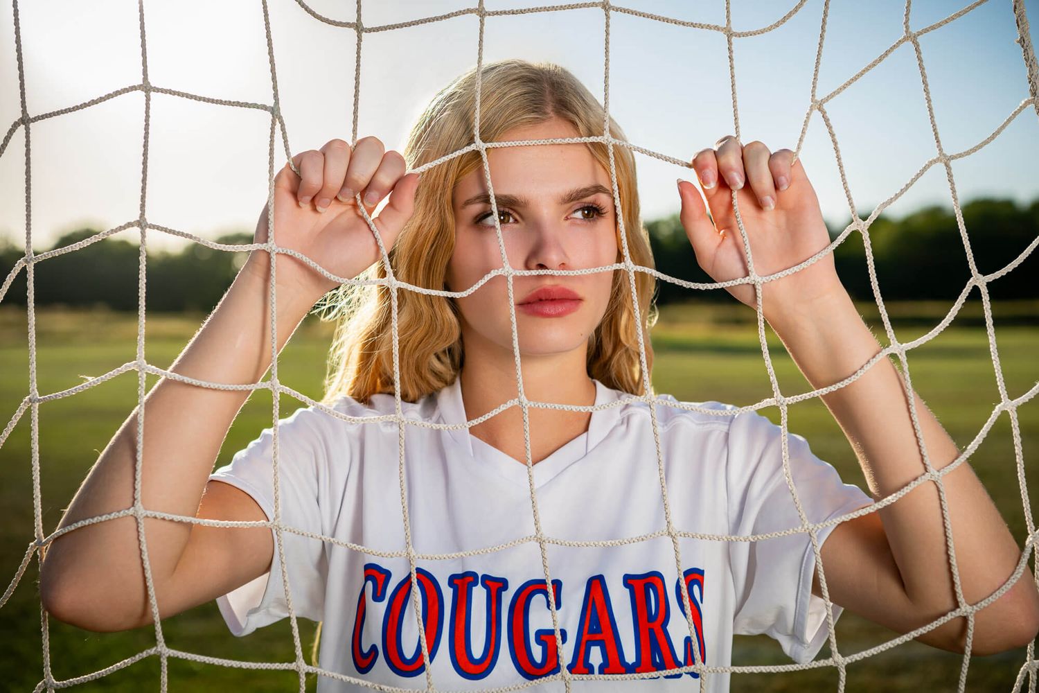 Athletes pose behind a soccer goal net during a sports photo session at sunset.