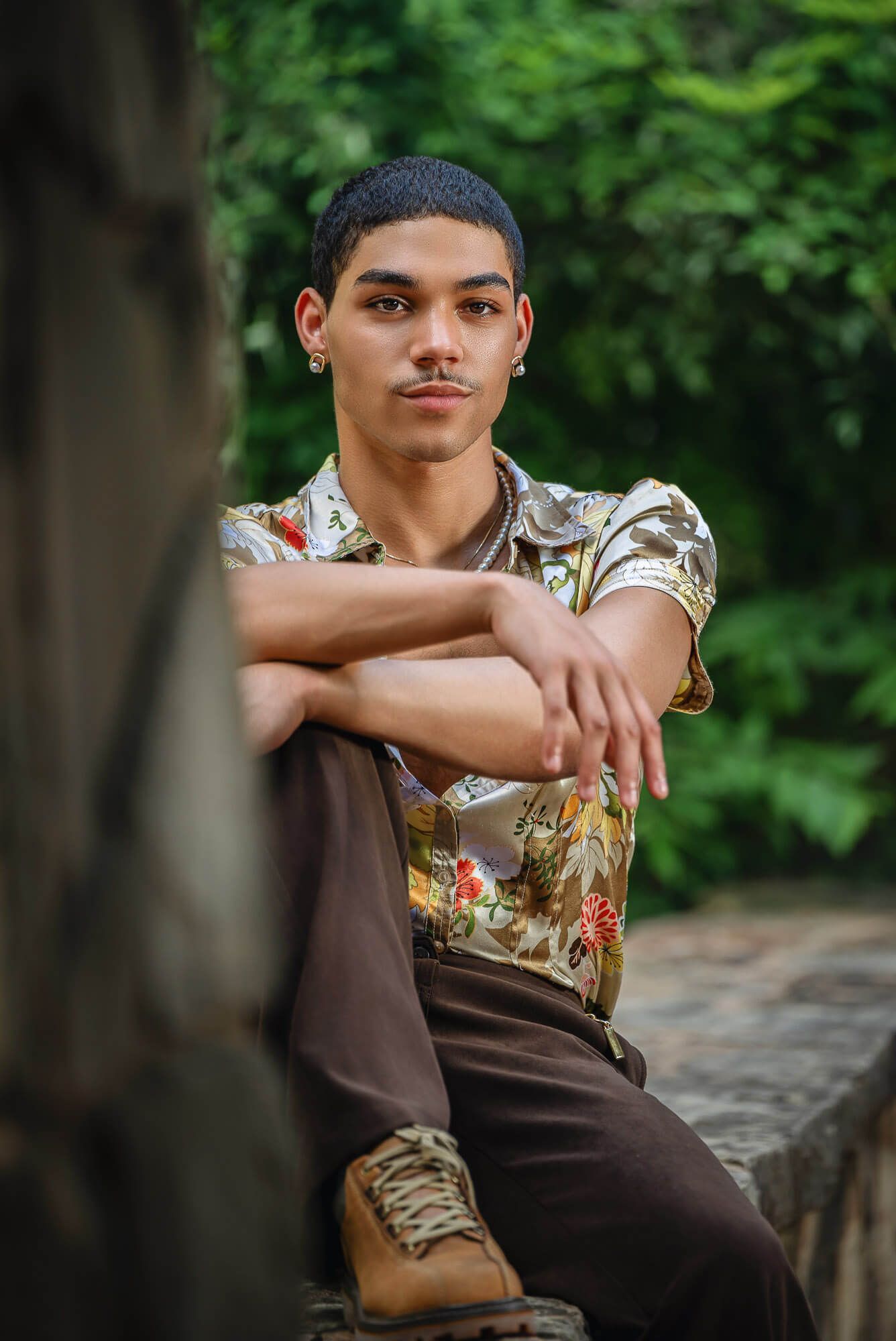 Male senior photography in Omaha of a black male sitting on a rock wall wearing a bright and colorful shirt.